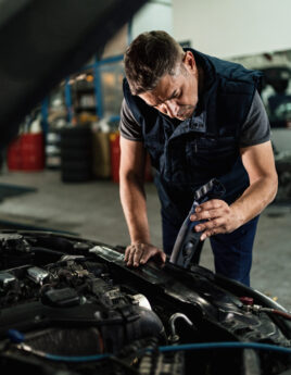 Auto mechanic using lamp while analyzing car engine in a workshop.