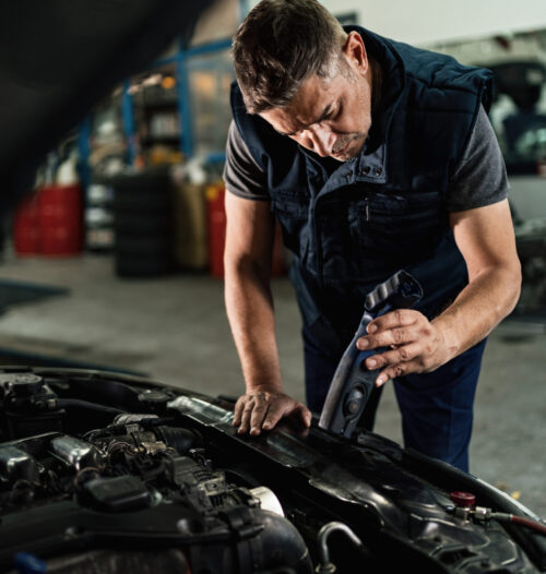 Auto mechanic using lamp while analyzing car engine in a workshop.